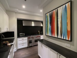 Black, white, and tan kitchen with a large colorful painting hung on the wall above white and black cabinets.