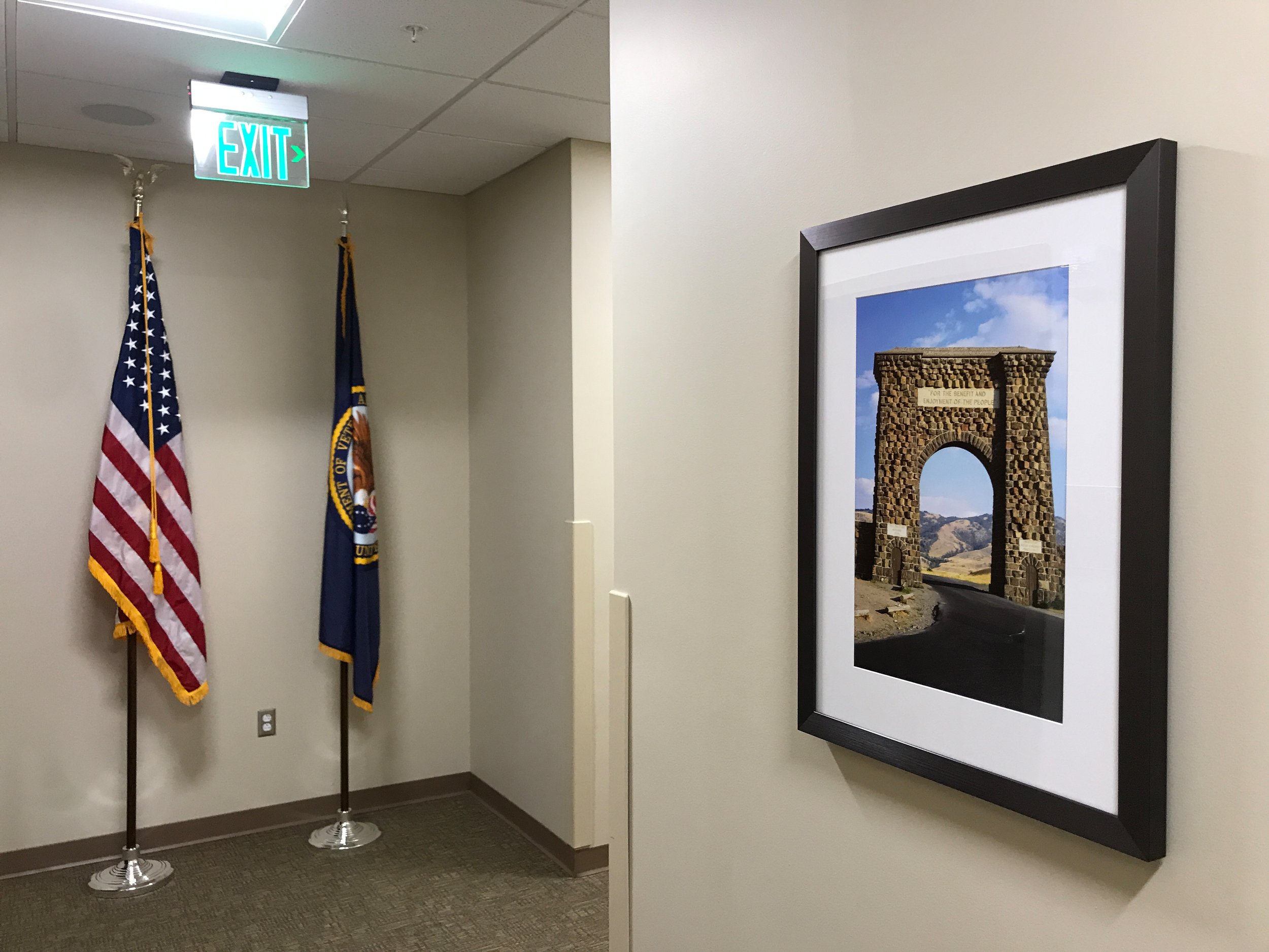 Peterson Picture's Government and GSA Framing services are specifically tailored for military bases, VA health care facilities and other government organizations. An example is this office building with two flags and floor stands, including an American flag and a Veterans flag. The opposite wall has a framed photo.