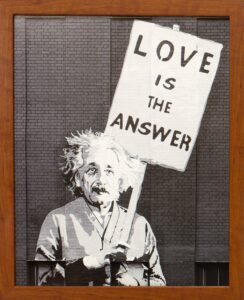 A wood-framed art piece of Albert Einstein holding a picket sign that reads "Love is the Answer."