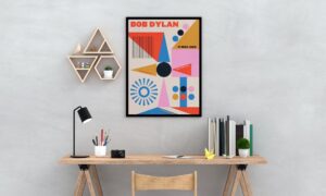 A wood studio desk with geometric wall art hung on the wall next to a geometric, colorful poster that says "Bob Dylan."