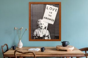 A kitchen table with a blue painted wall in the foreground with a framed art piece of Albert Einstein holding a "Love is the Answer" sign.