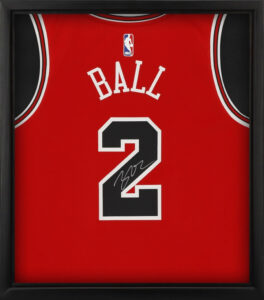 A signed red basketball jersey is neatly framed in a black frame. The jersey is for player Ball and his number 2.