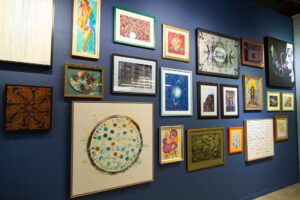A zoomed-out image of a blue-painted wall features a variety of framed art pieces in all different colored frames.