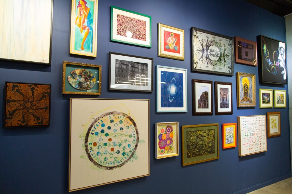 A gallery art wall features several pieces placed all over a blue-painted wall. Each art piece has a different style and color frame.
