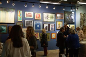 People gather in the Peterson Picture Co. in-house art gallery, looking at art beautifully framed in various picture frames that cover the blue painted walls.