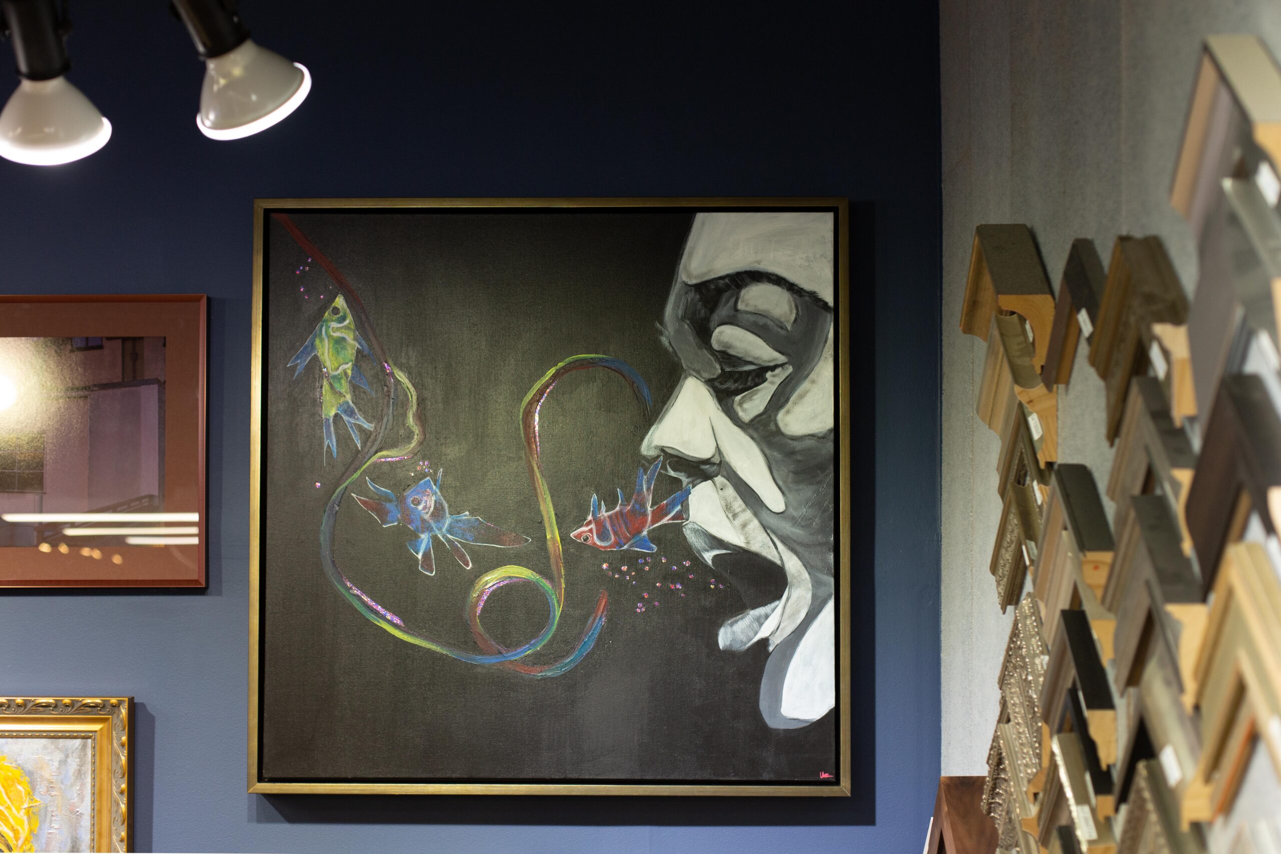 A large square art piece hangs on the wall of the in-house Peterson Picture Co. gallery. The art shows the profile of a face with fish swimming around.