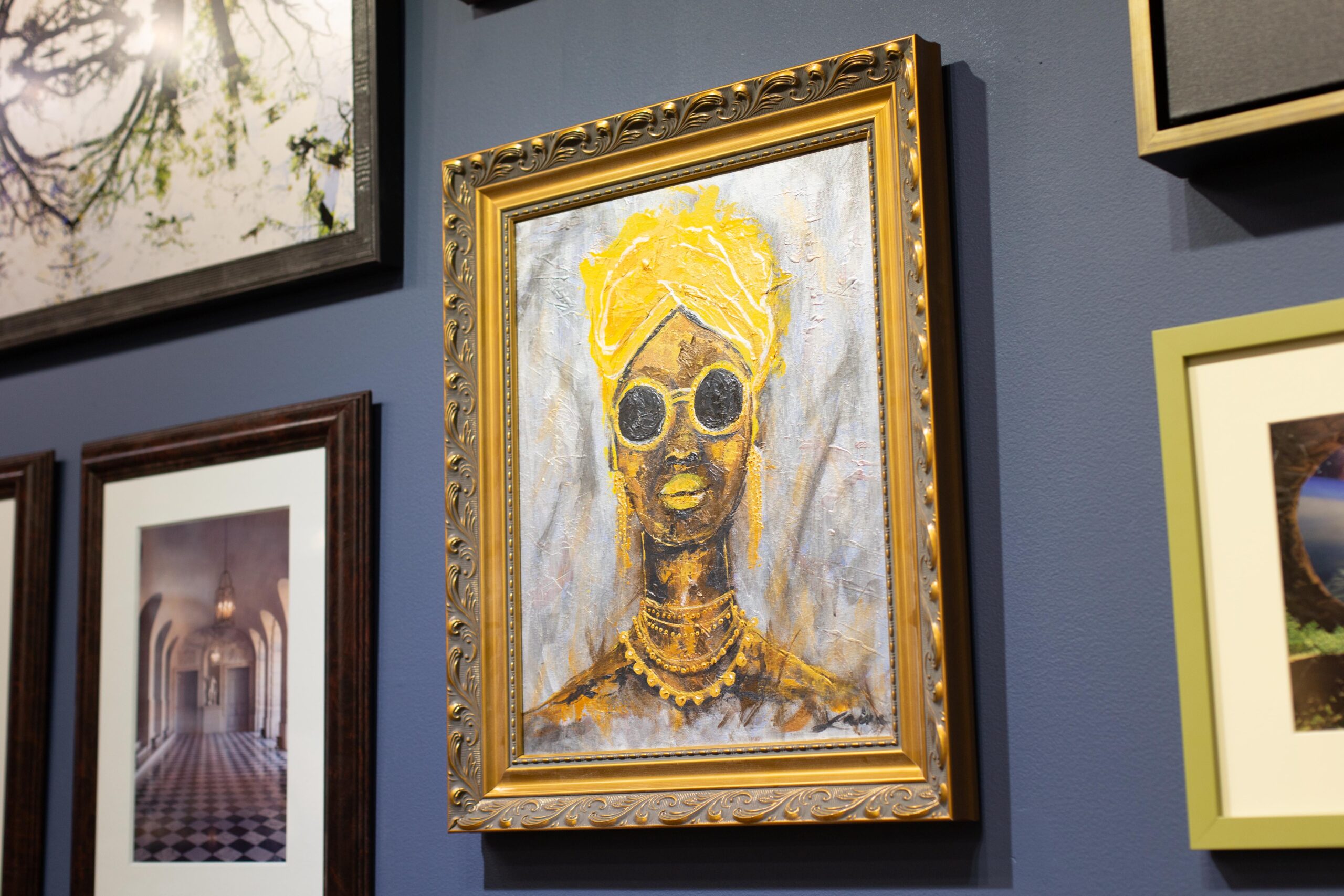 A closeup angle shows three pieces of art, focusing on the painting of a woman in an elegant gold frame. The art hangs in the Peterson Picture Co. gallery.