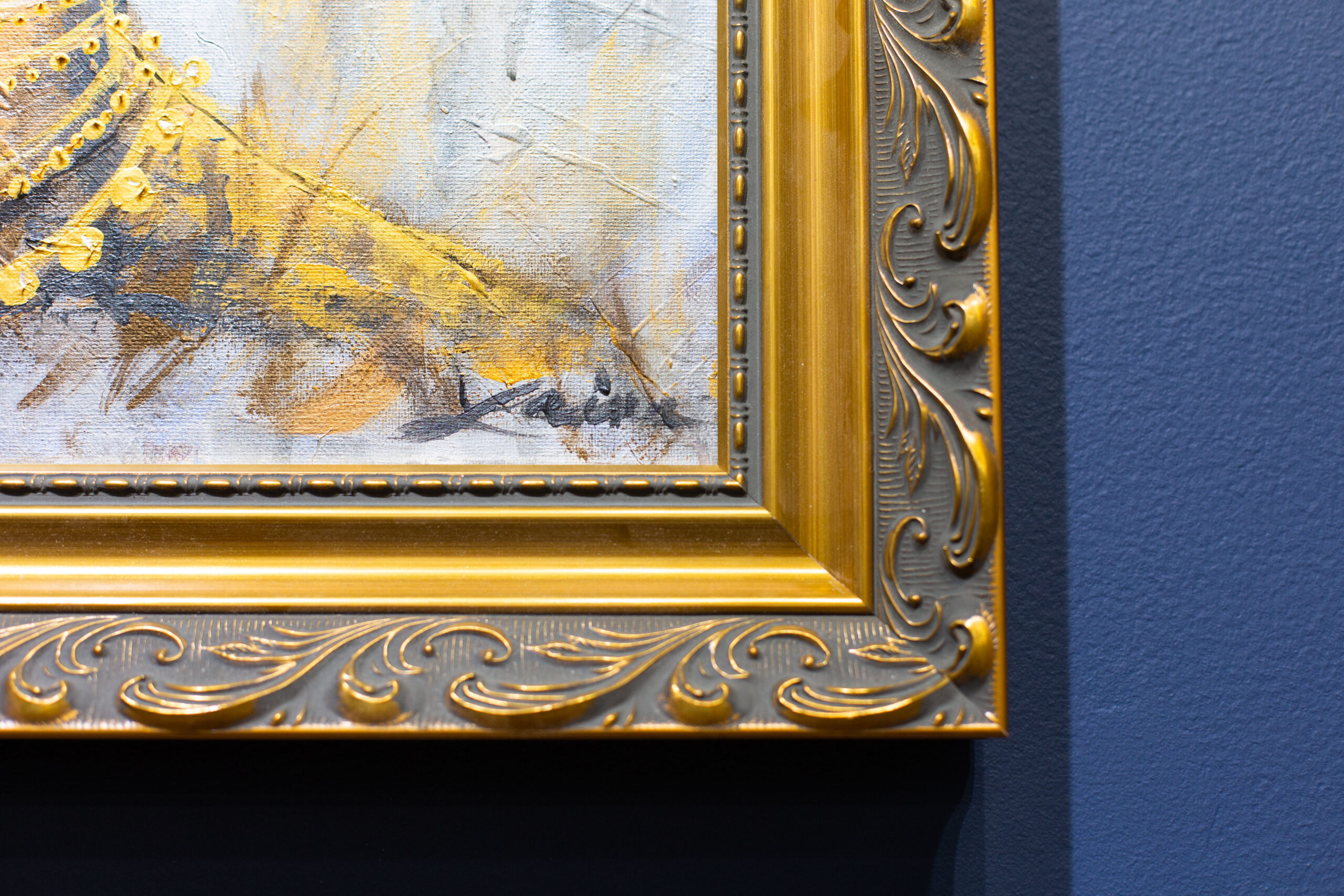 A tight closeup shows the corner of an elegant gold frame with a painting of a woman. The art hangs in the Peterson Picture Co. gallery.