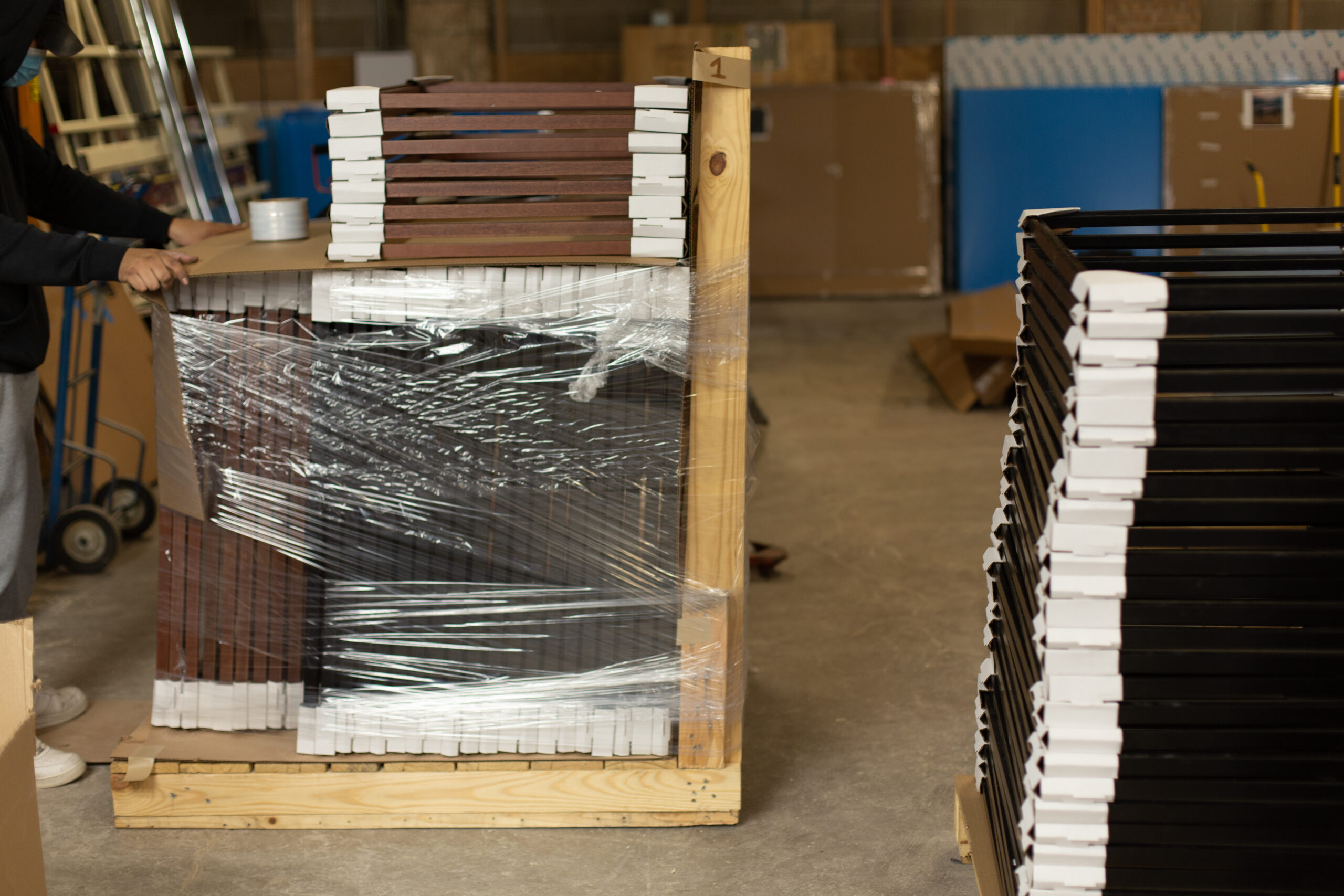 A worker with a wooden palette with stacks of wooden frames, ready for use and delivery. Peterson Picture Co. offers secure delivery and installation services.
