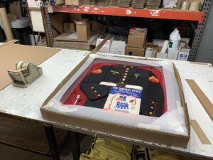 An example of Peterson Picture fullfillment framing project - a zoomed-out image of a custom framing of a Marine Corps jacket is nicely packaged and ready for delivery. The pressed jacket is delicately laid in the frame.