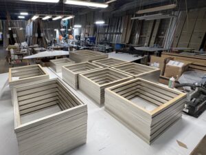 Zoomed-out image of several stacks of neatly organized light, tan natural wood frames line the workshop floor. The frames - a complete commercial order by Peterson Picture Co.