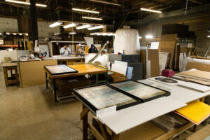 Three oversized, colorful abstract art pieces are framed and placed on a table in the Peterson Picture Co. facility. Each frame is carefully assembled.